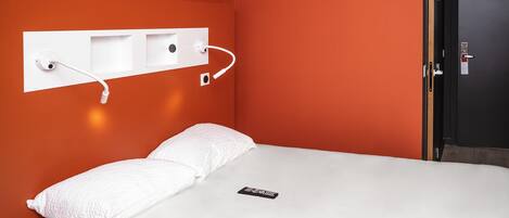 Una habitación de hotel moderna con una cama grande, ropa de cama blanca y una estación de carga en la pared.
