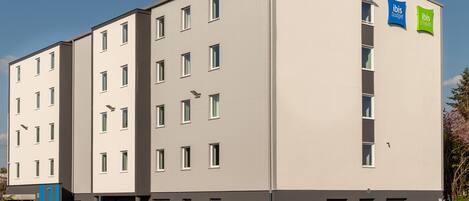 A multi-story hotel with a flat facade, several windows, and a parking lot with cars.