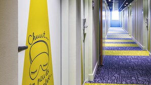 Pasillo de hotel con alfombra estampada, puertas y una pared con un gráfico y texto.