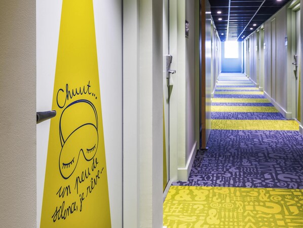 Pasillo de hotel con alfombra estampada, puertas y una pared con un gráfico y texto.