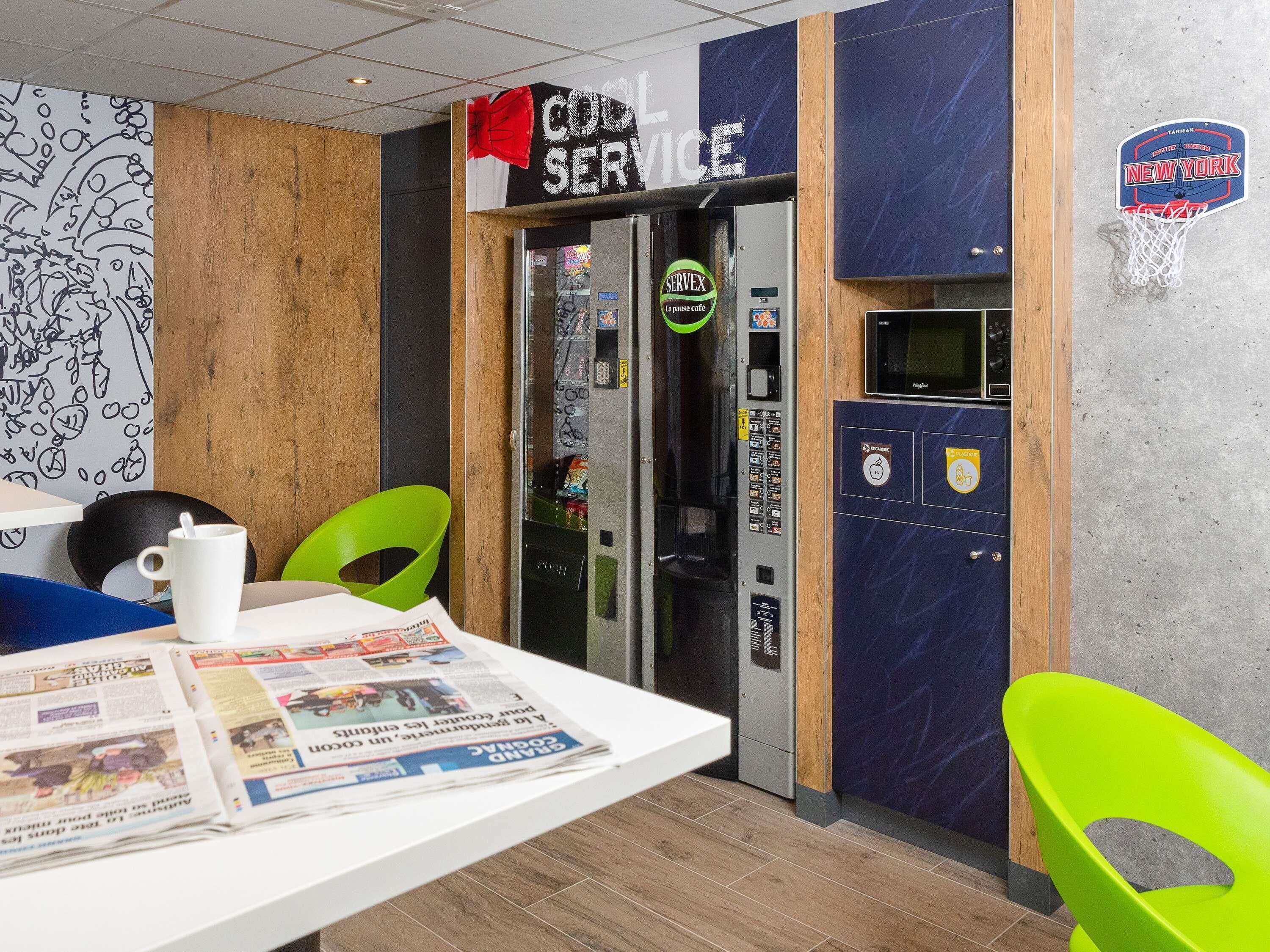 A cafe area with a coffee machine, a newspaper rack, and a wall with a basketball hoop.
