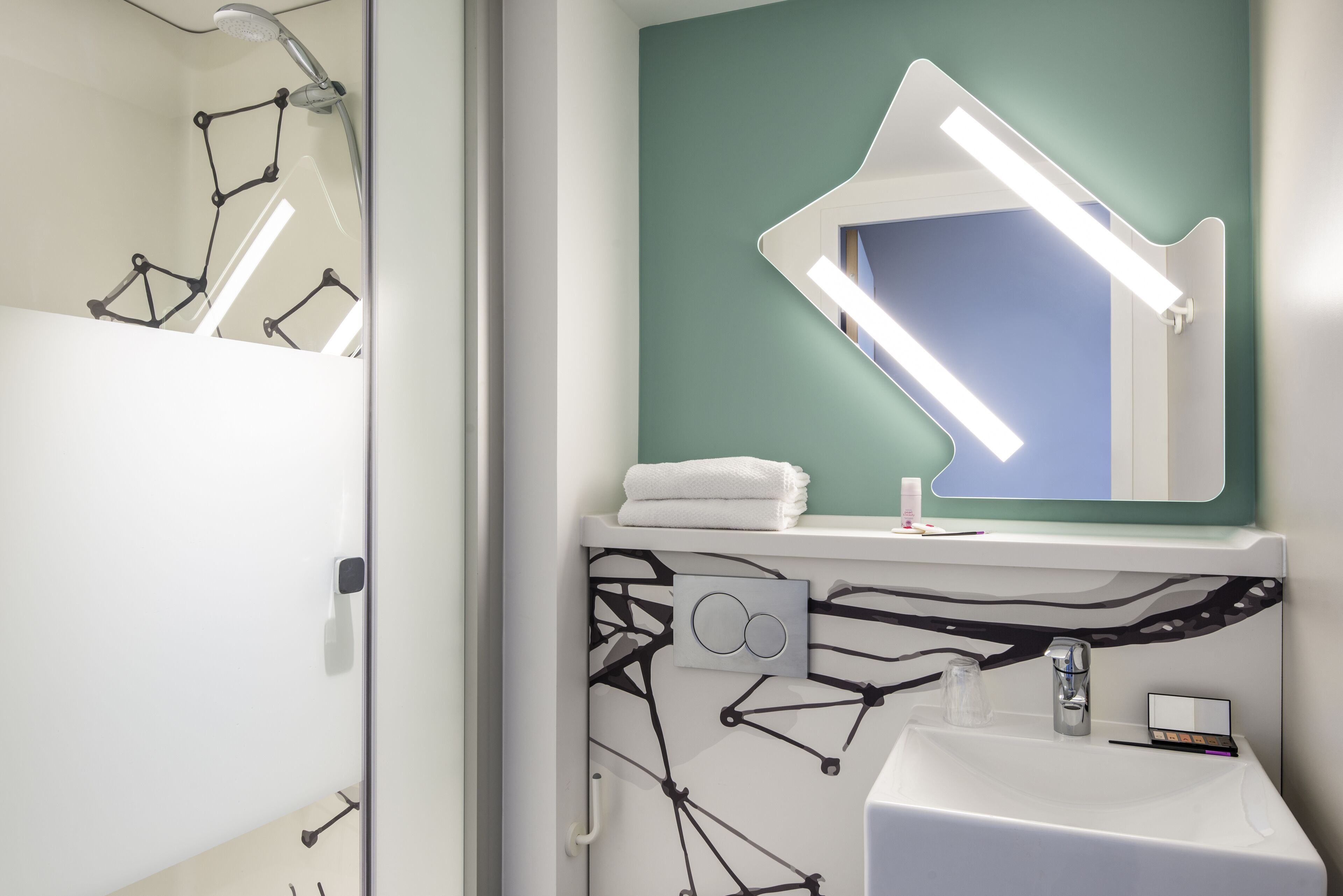Un baño moderno con un lavabo blanco, un espejo con diseño geométrico y una zona de ducha.