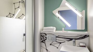 Un baño moderno con un lavabo blanco, un espejo con diseño geométrico y una zona de ducha.