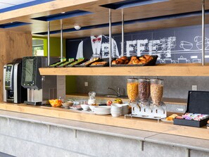 Buffet com diversos alimentos, máquina de café e dispensador de bebidas.