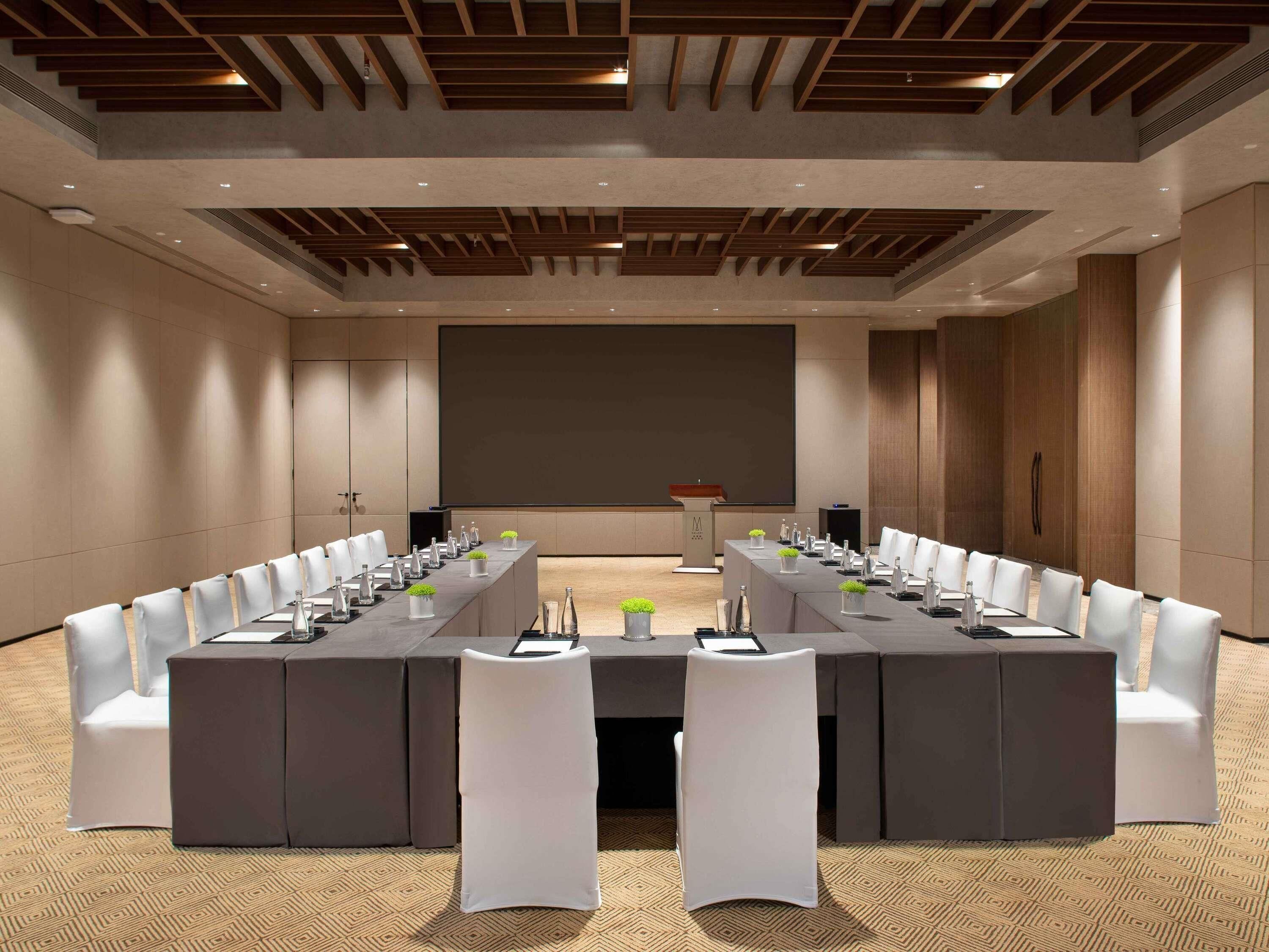 Een vergaderzaal met een lange tafel, witte stoelen en een spreekgestoelte.