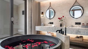 Une salle de bain moderne avec une grande baignoire, deux miroirs, un meuble-lavabo et un grand lavabo circulaire orné de pétales rouges.
