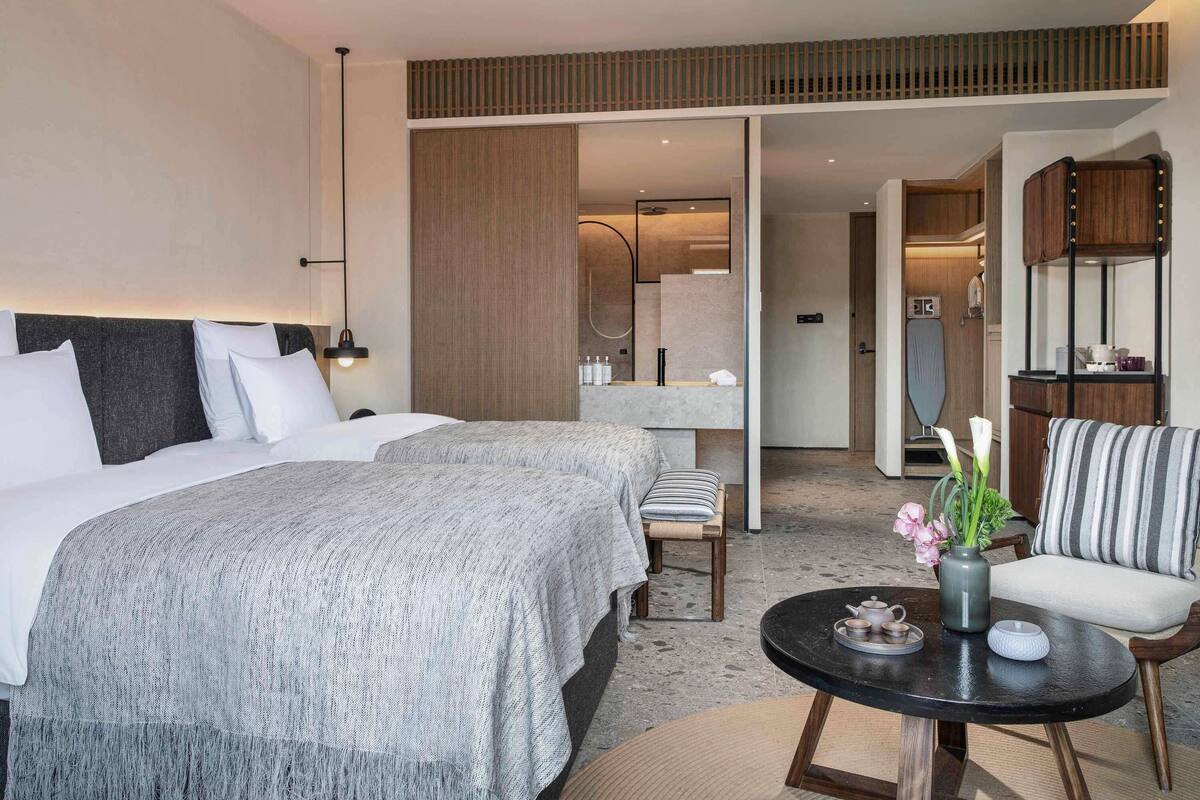 A modern hotel room with a large bed, a small round table with tea set, a chair, and a view of the bathroom.