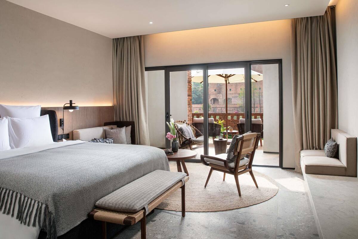 Una habitación de hotel moderna con una cama grande, una zona de estar con una mesa y sillas, y un balcón con vistas al exterior.