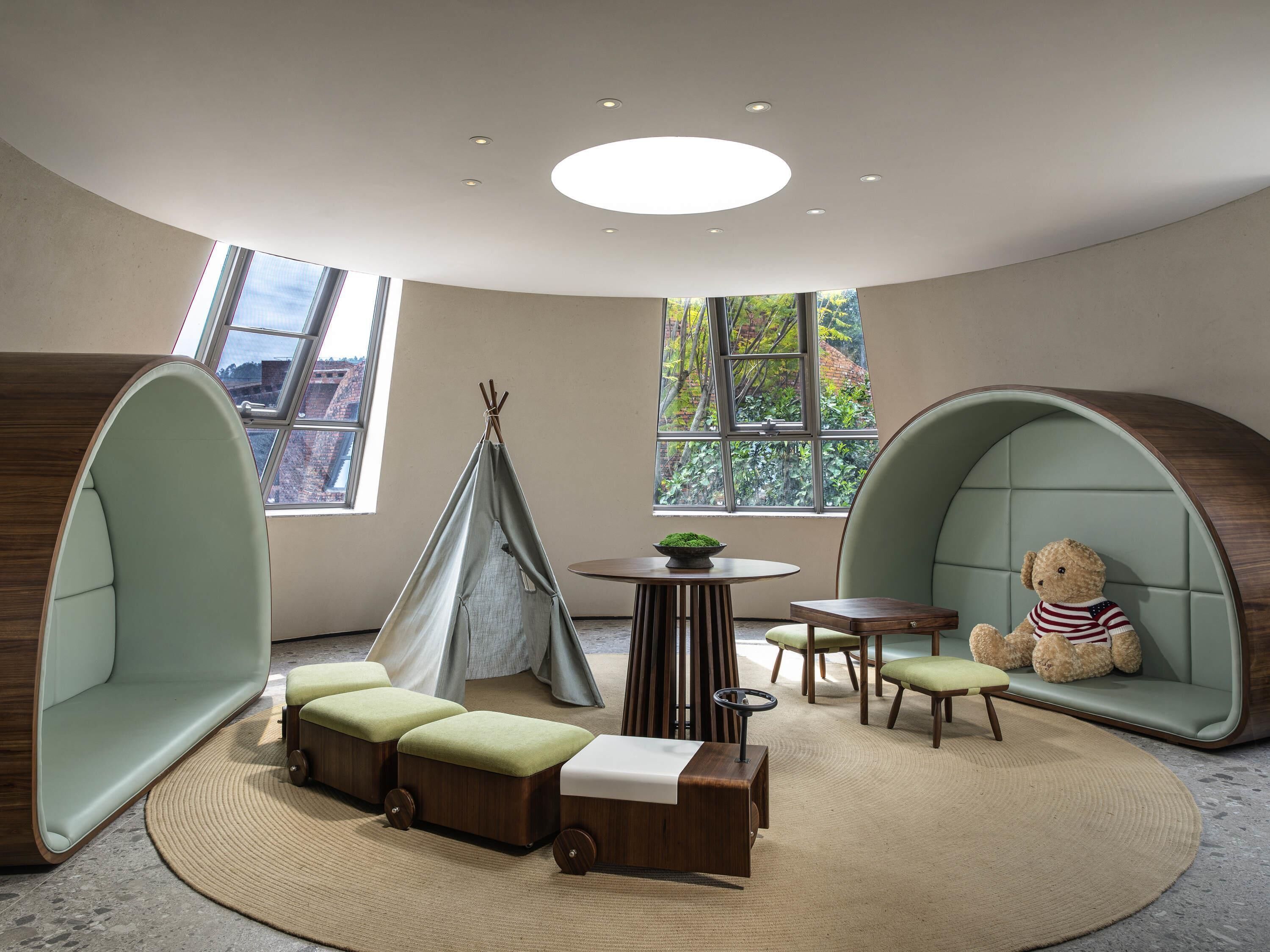 A cozy room with a circular seating area, a small table with a bowl, and a teddy bear on a cushioned bench.