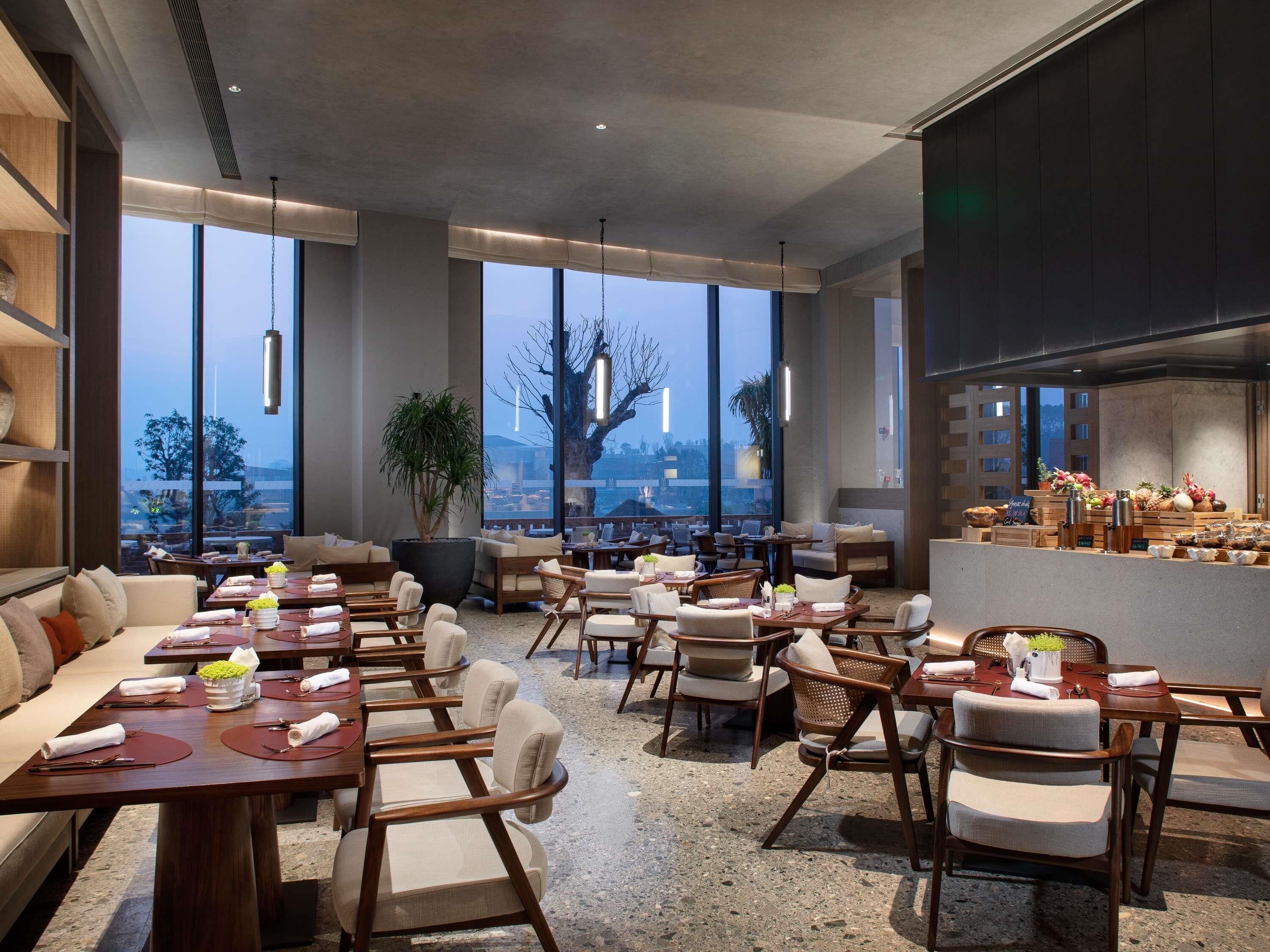 A modern restaurant with high ceilings, large windows, and a variety of seating arrangements.