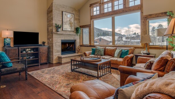 A spacious living room with a fireplace, leather furniture, and a large window offering a mountain view.
