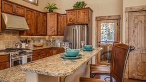 A kitchen with wooden cabinets, a stainless steel refrigerator, granite countertops, and a dining area with a chair and table.