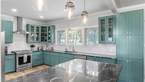 Une cuisine moderne avec des meubles de couleur turquoise, un grand îlot en marbre, des appareils électroménagers en acier inoxydable et des luminaires suspendus.