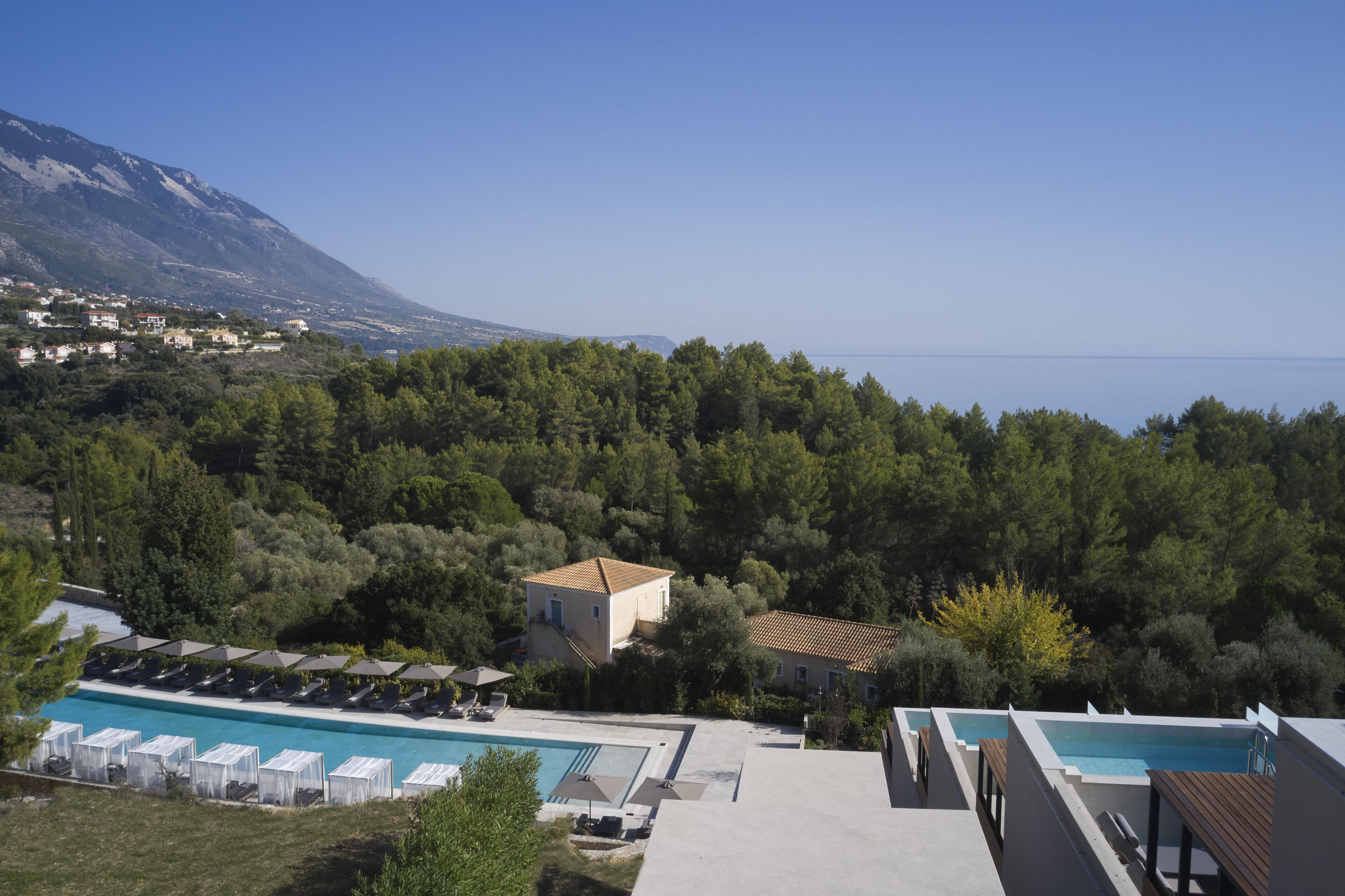 A resort with a pool, lounge chairs, and a view of the sea and mountains.