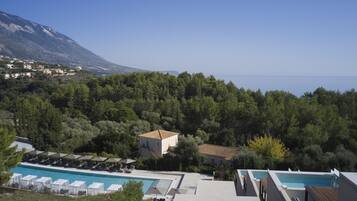 A resort with a pool, lounge chairs, and a view of the sea and mountains.
