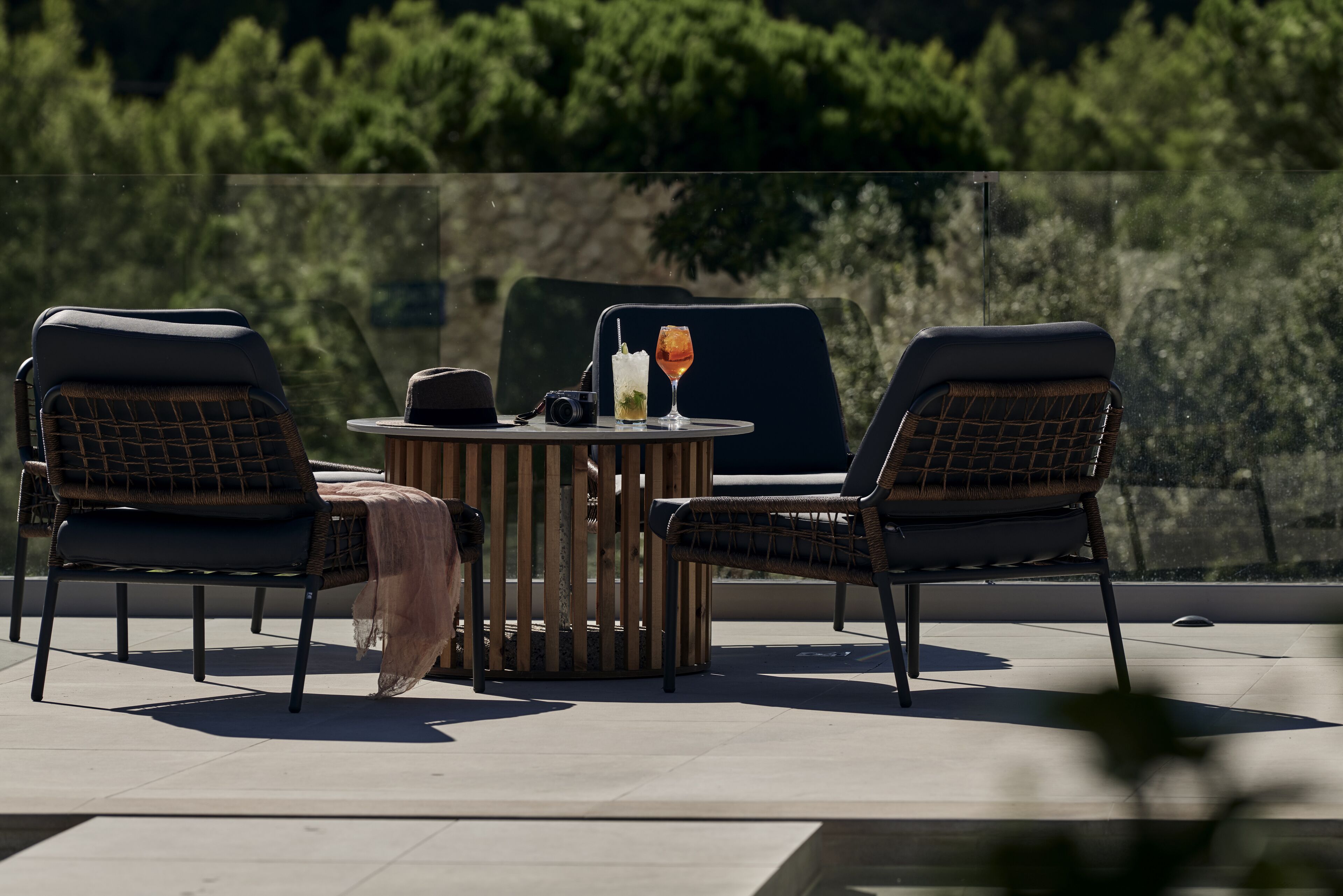 A terrace with two wicker chairs, a round wooden table, and a glass partition.