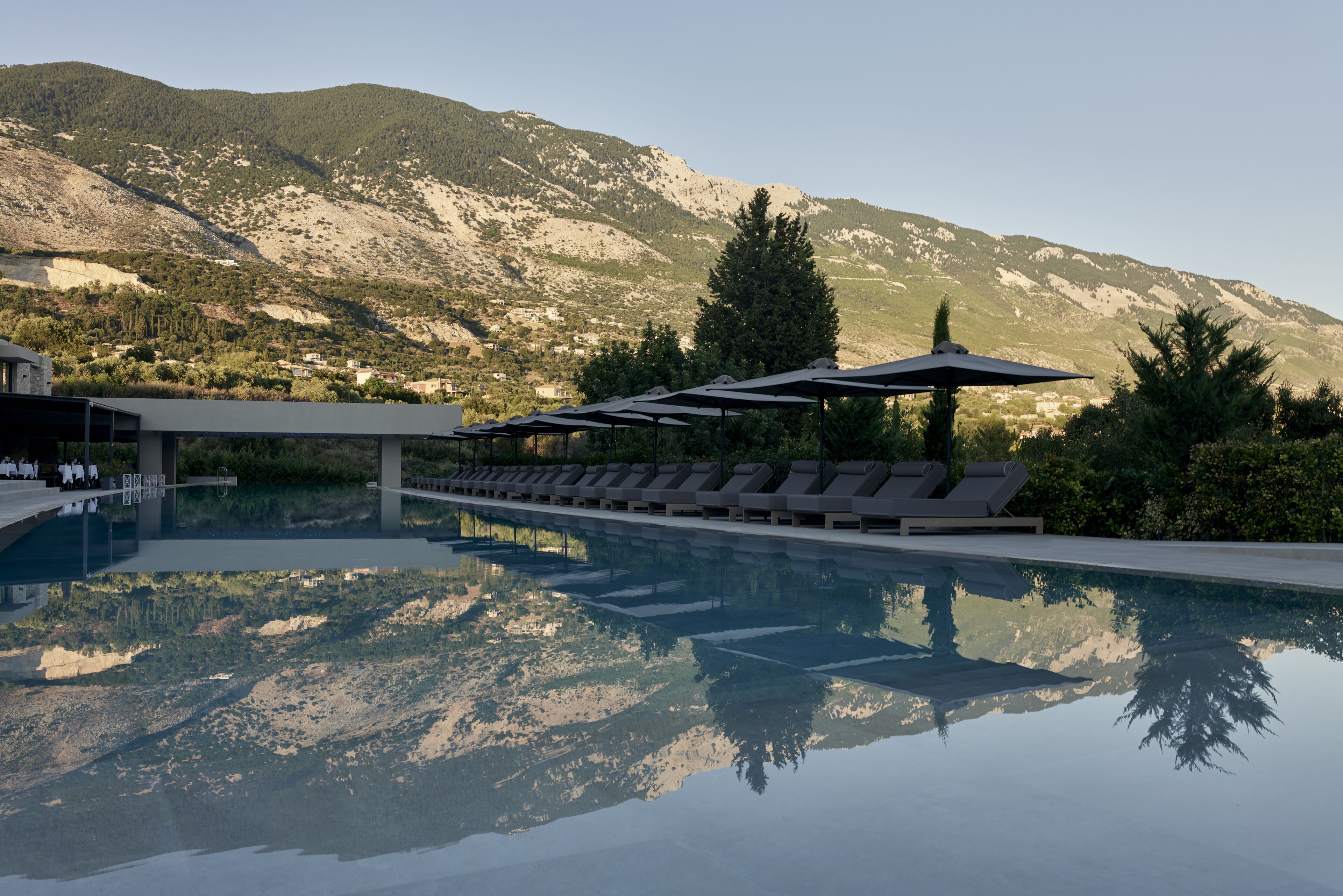 Una piscina con sillas de descanso y sombrillas, rodeada de montañas.