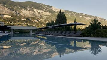 Una piscina con sillas de descanso y sombrillas, rodeada de montañas.