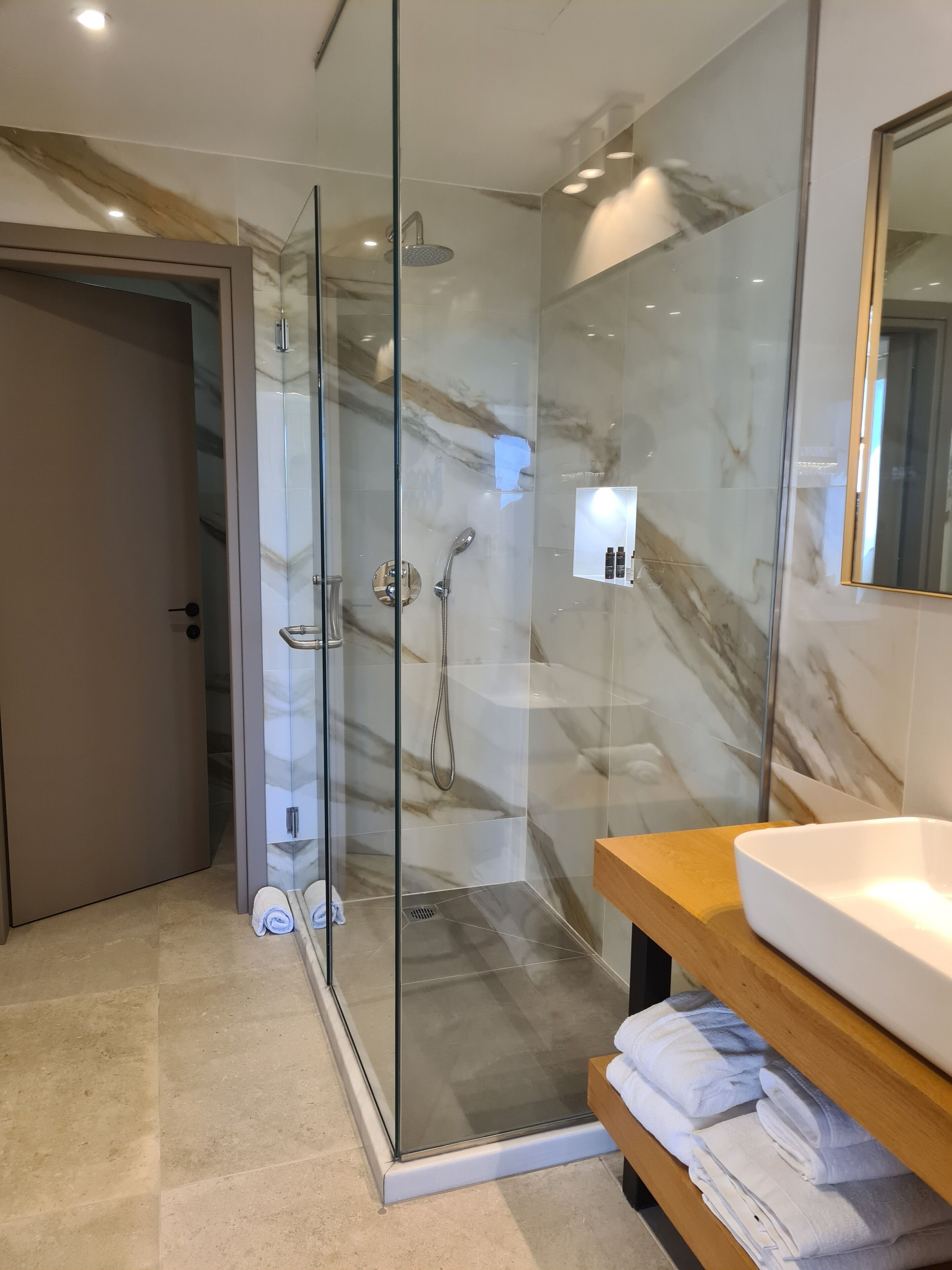 Une salle de bain moderne avec une douche à parois de verre, un mur recouvert de carreaux de marbre et un meuble-lavabo en bois.