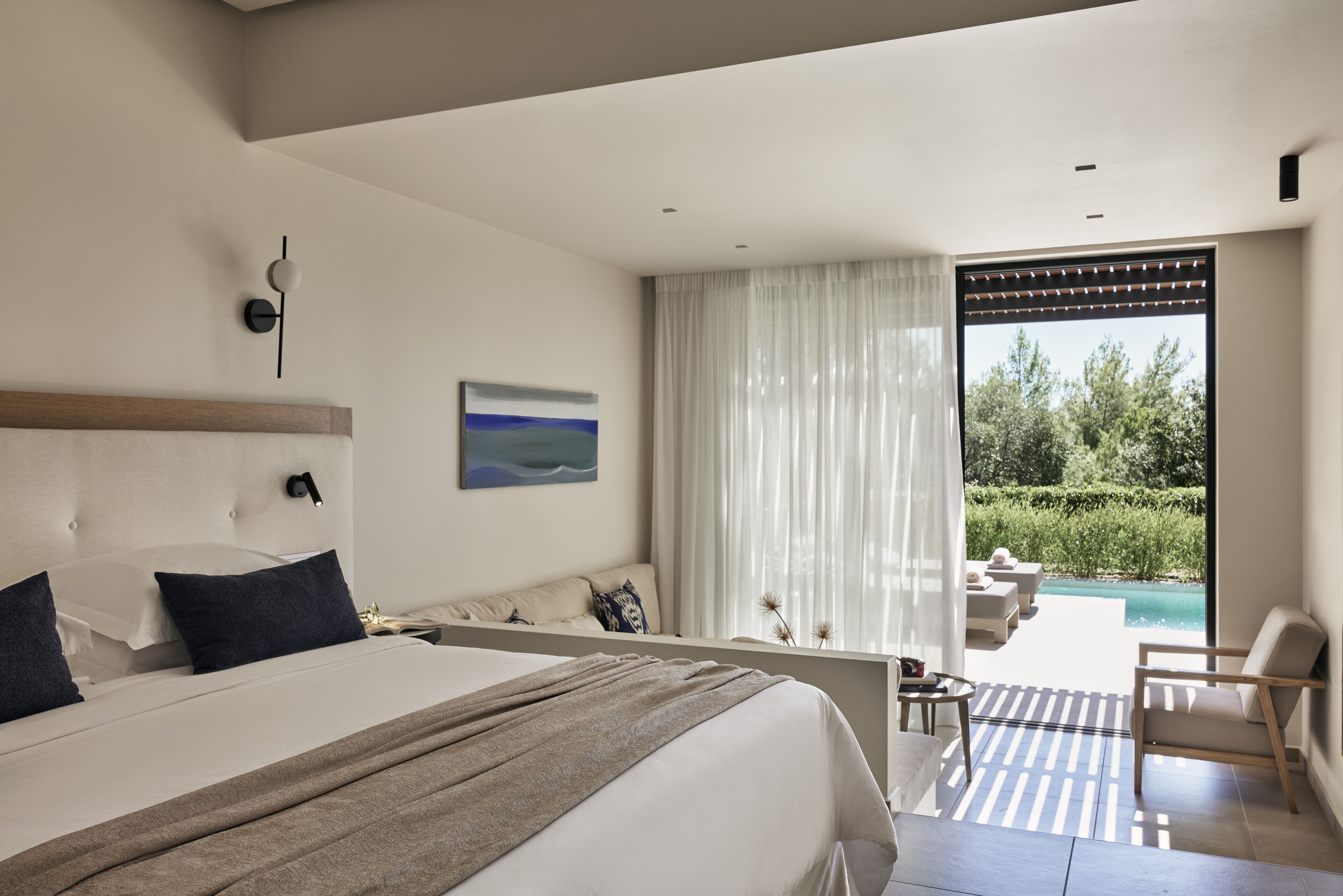 Ein modernes Hotelzimmer mit einem großen Bett, Blick auf einen Swimmingpool und einem Balkon mit Sitzgelegenheit.