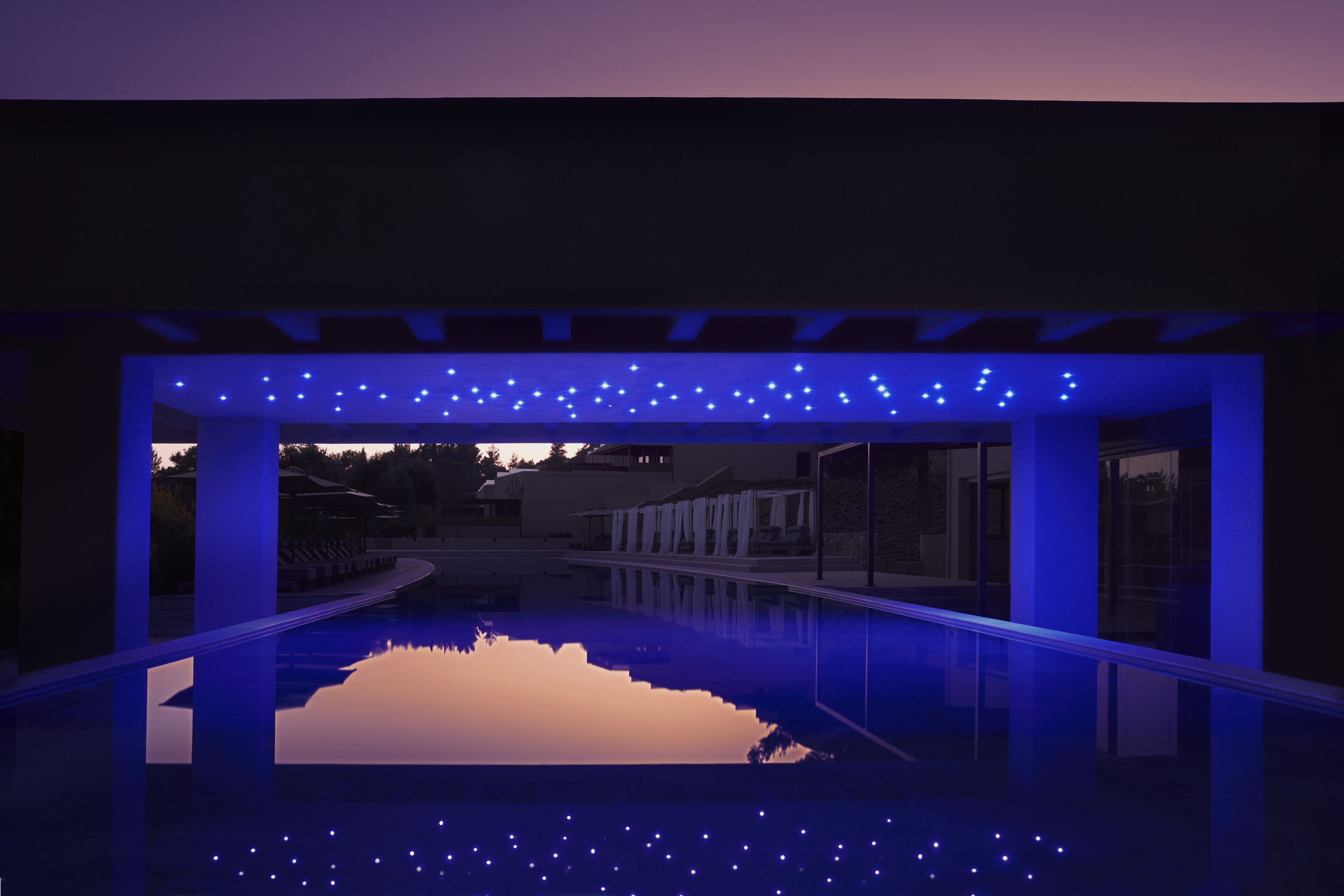 An indoor swimming pool with a clear view of the surrounding buildings and a sunset in the background.