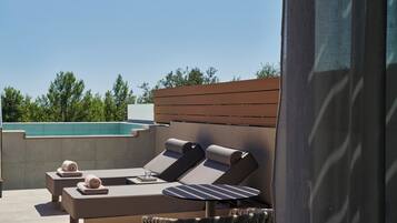 A rooftop lounge area with sun loungers, a small table, and a view of a swimming pool.