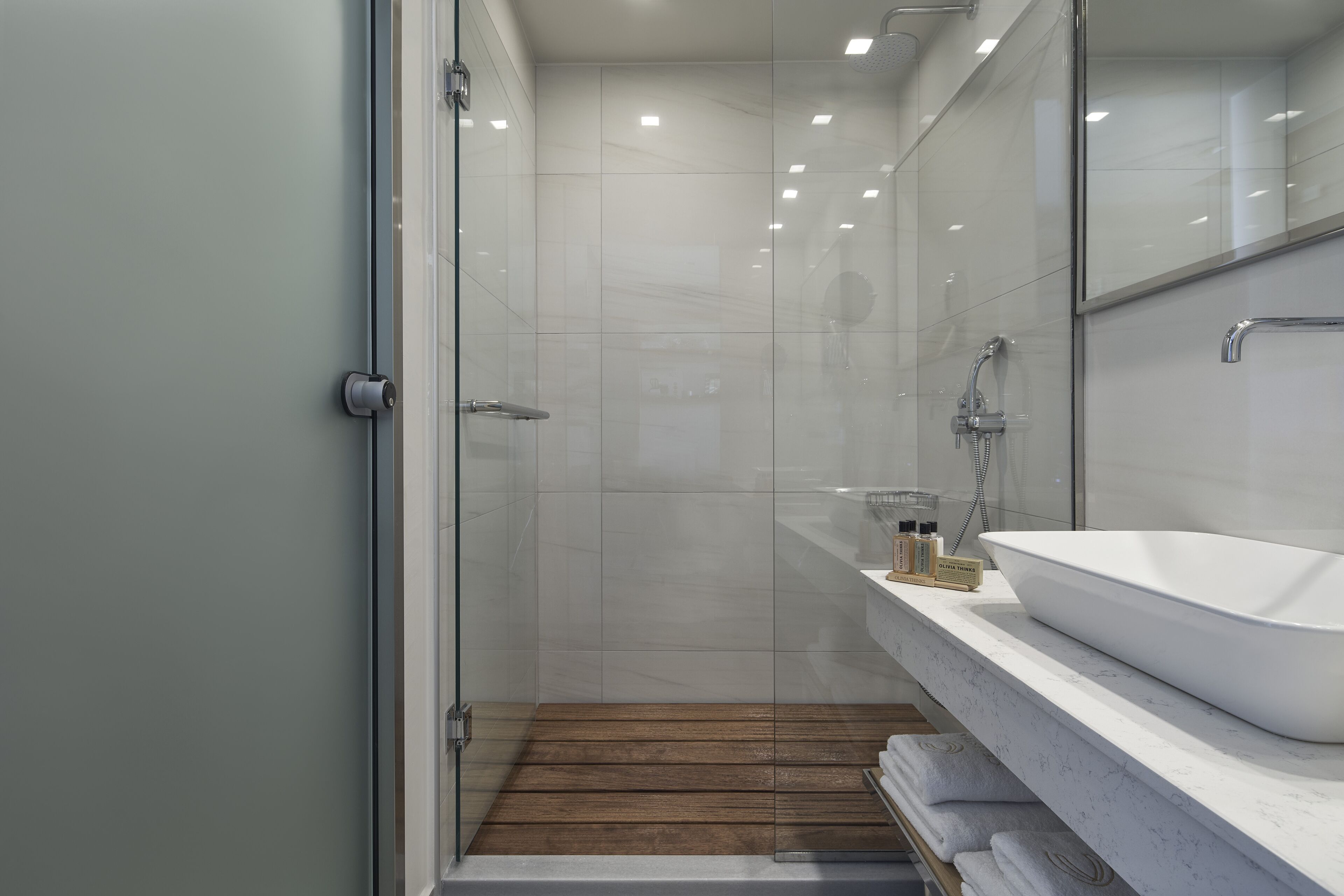 A modern bathroom with a glass shower enclosure, a white sink, and a wooden floor.