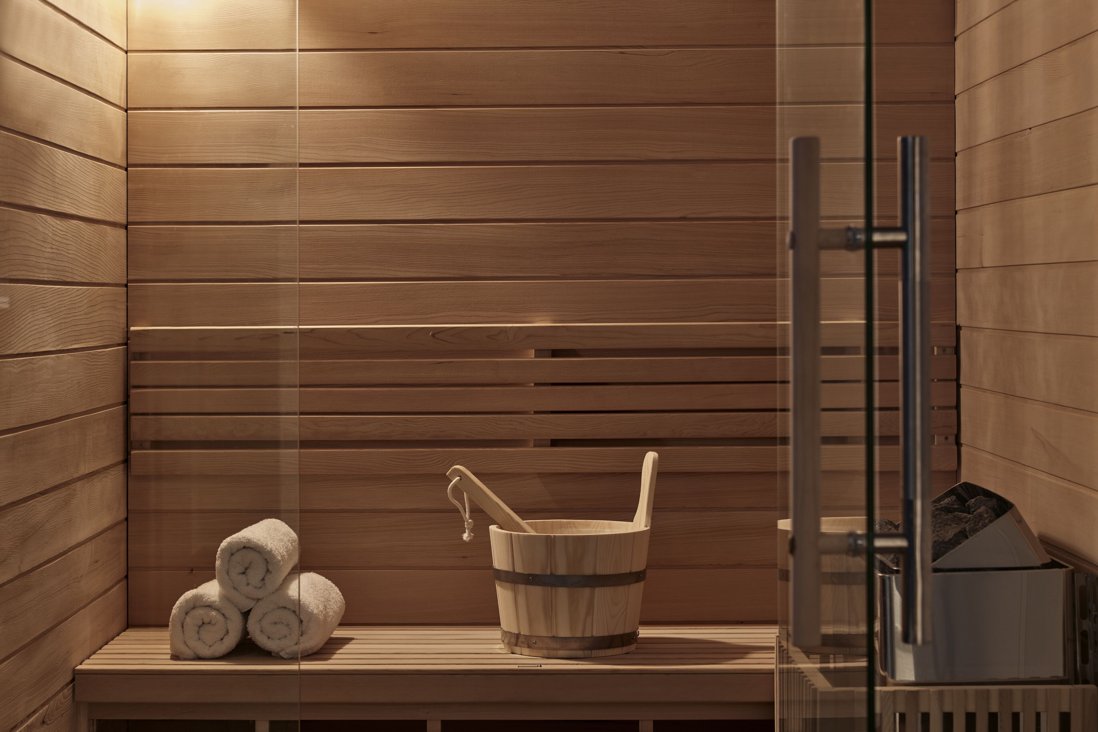 A sauna with wooden benches, a wooden bucket with a ladle, and rolled towels.