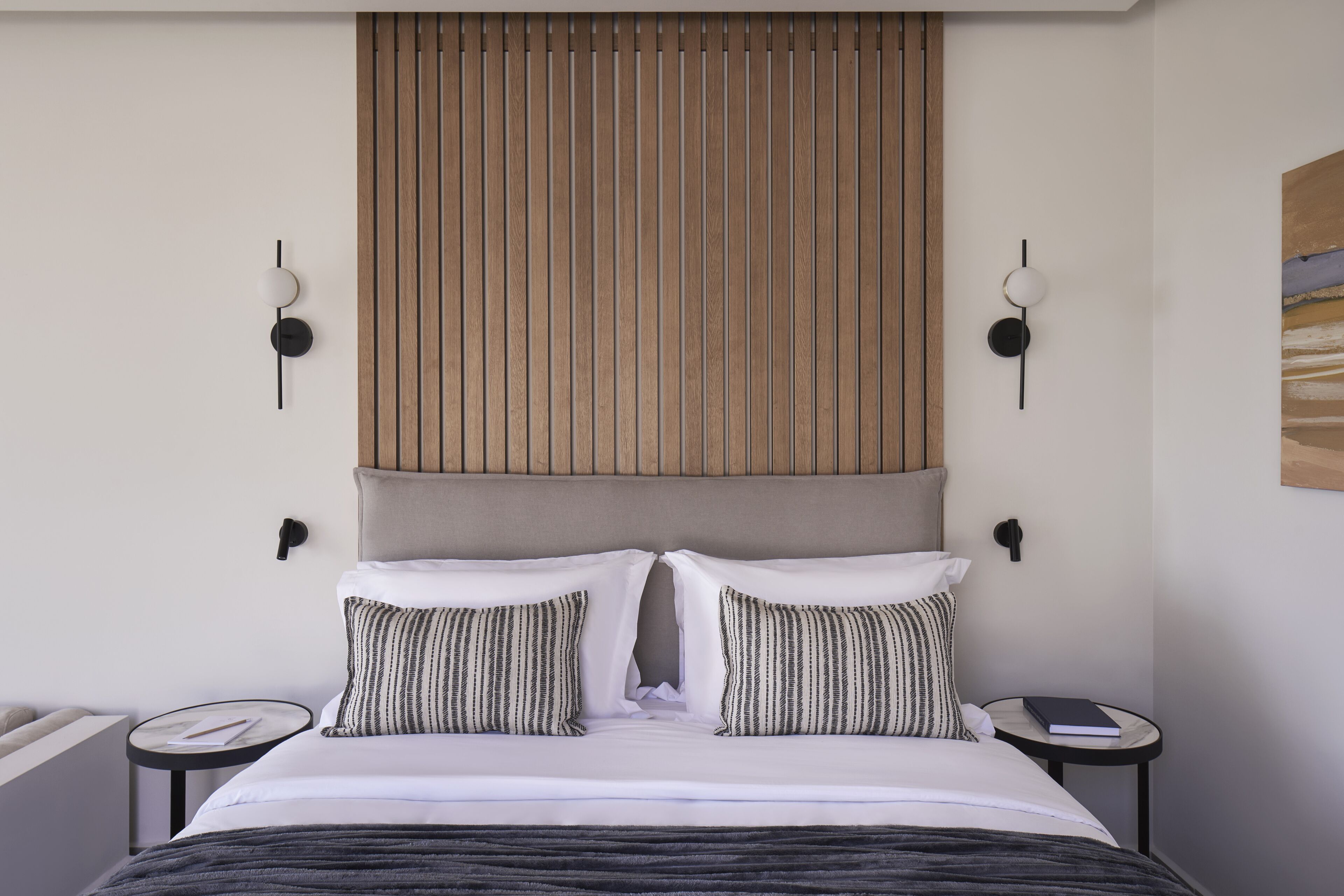A modern hotel room with a large bed, two bedside tables, a wooden headboard, and a wall-mounted light fixture.