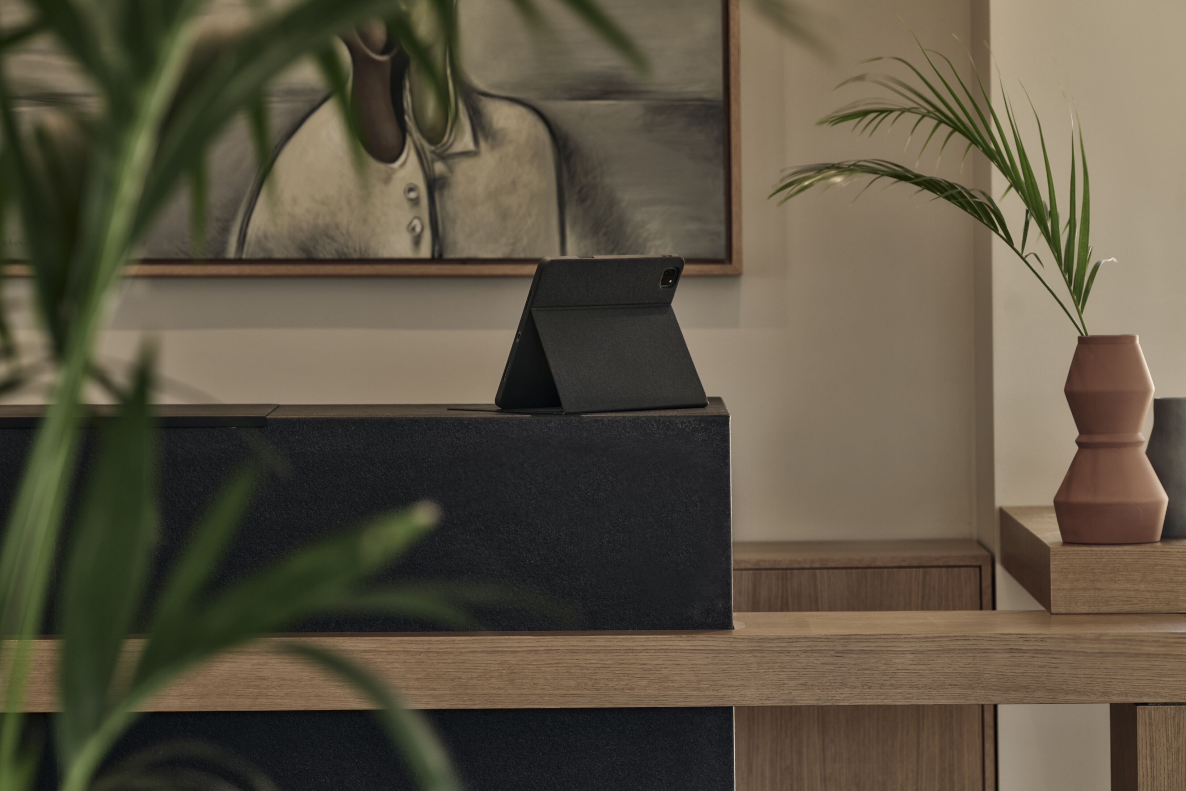 Un comptoir d’accueil avec une tablette, un portrait encadré et une plante en pot.