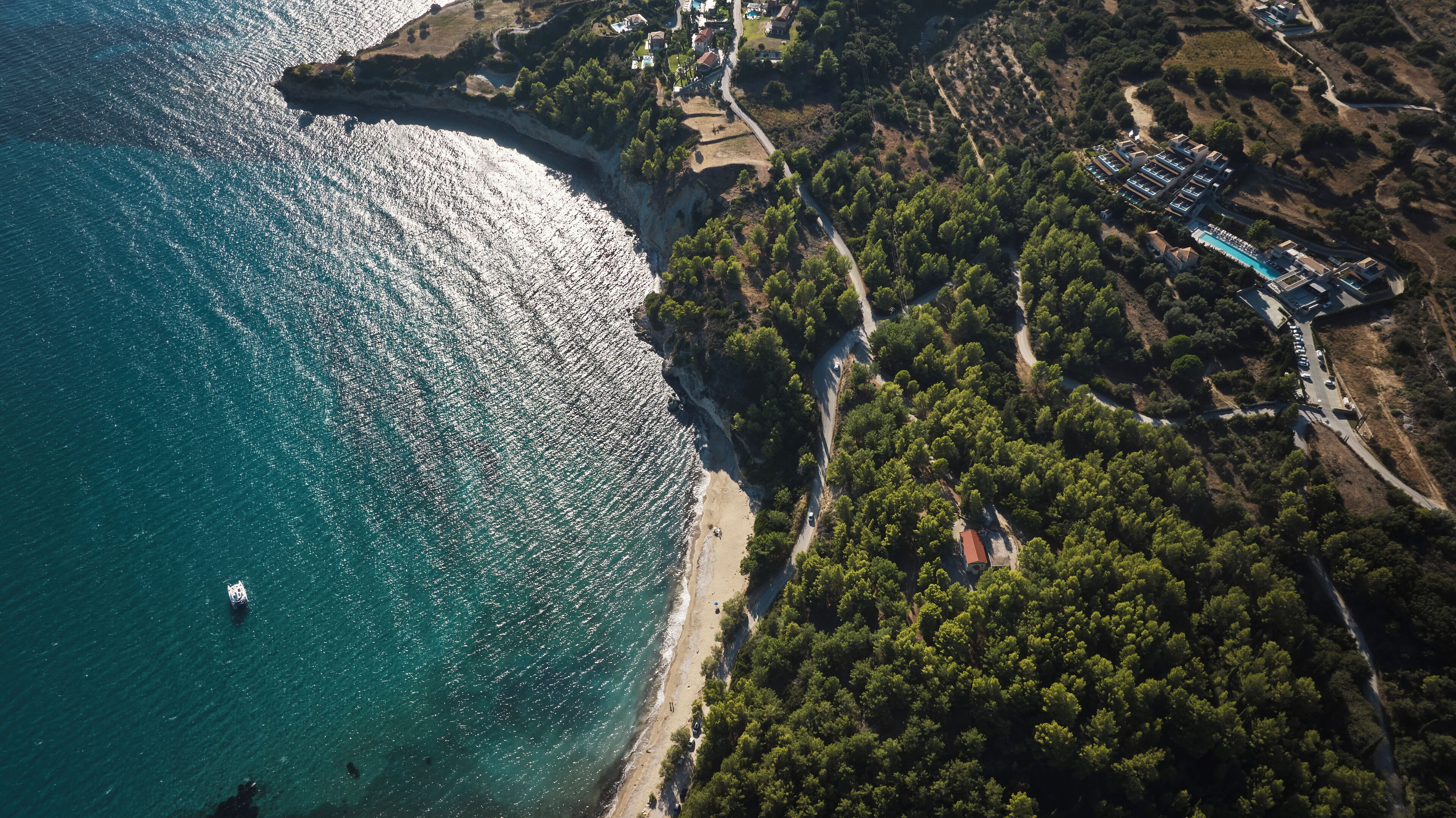An aerial view of a coastal area with a beach, a road, and a resort with multiple buildings.