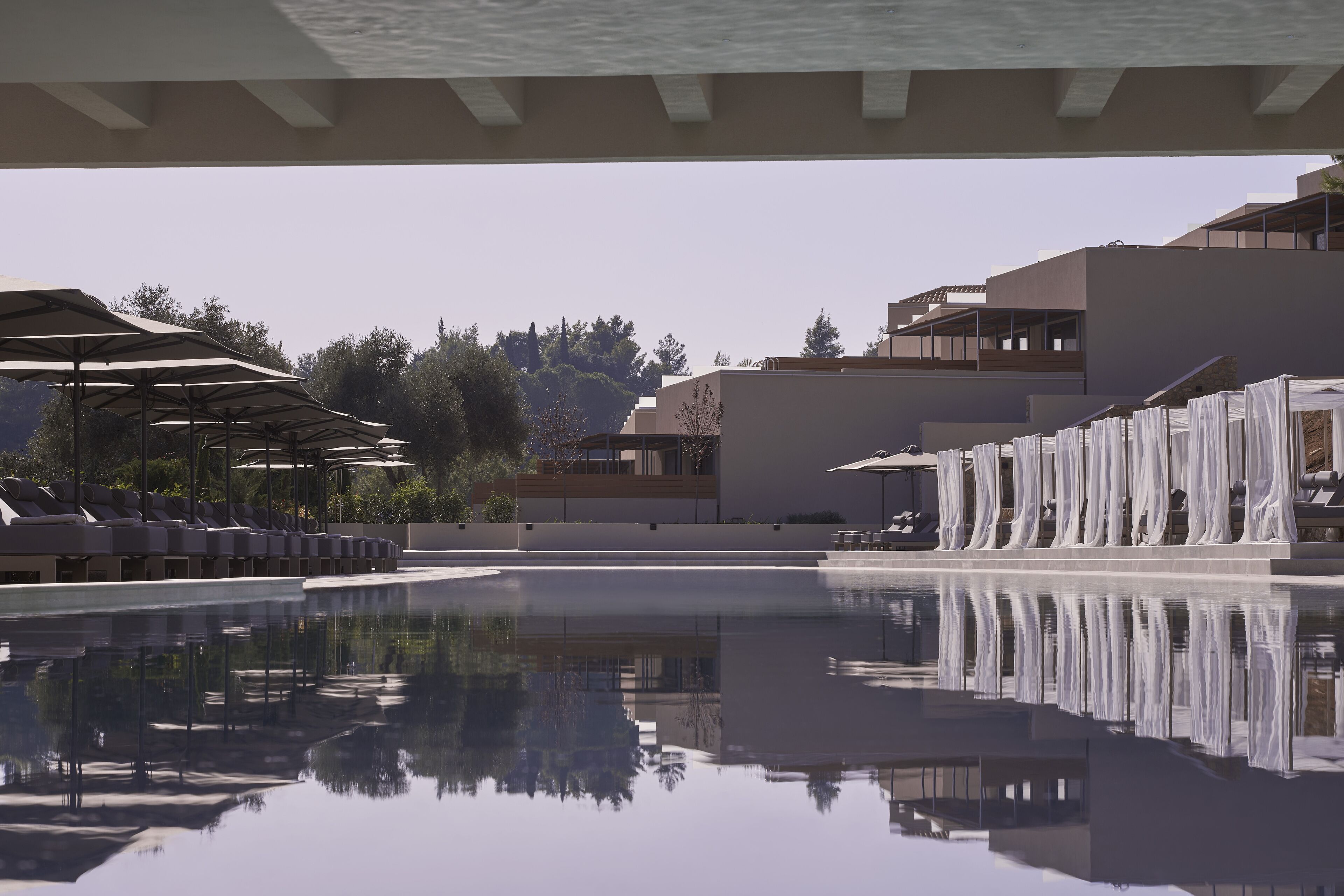 A modern pool area with lounge chairs and umbrellas, surrounded by contemporary buildings and trees.