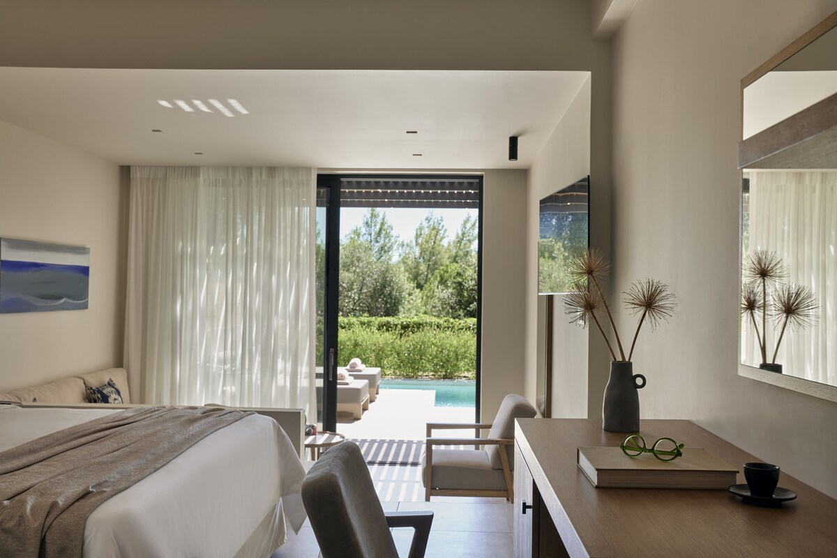 A modern bedroom with a bed, a desk, and a view of an outdoor pool area.