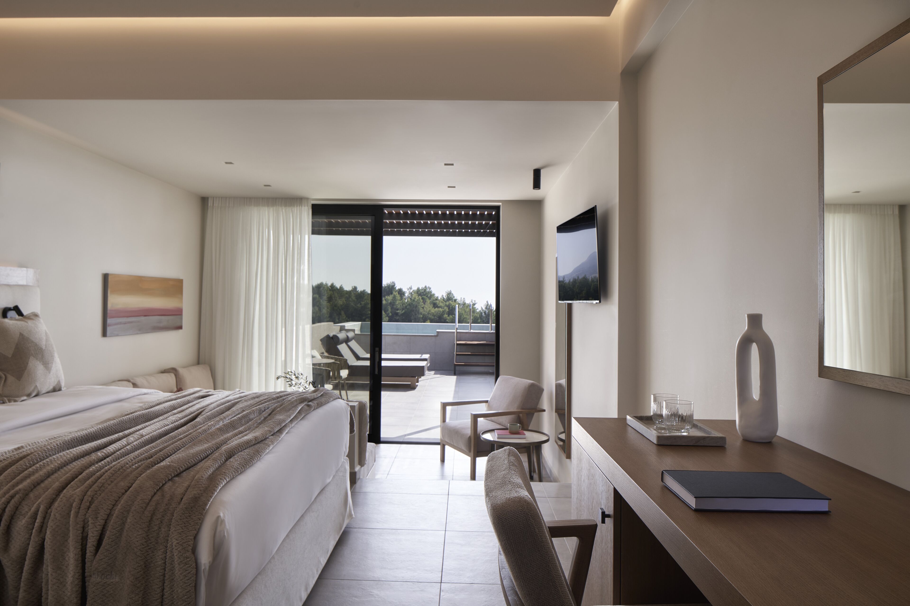 Una habitación de hotel moderna con cama, escritorio, silla, televisor y vistas al exterior.