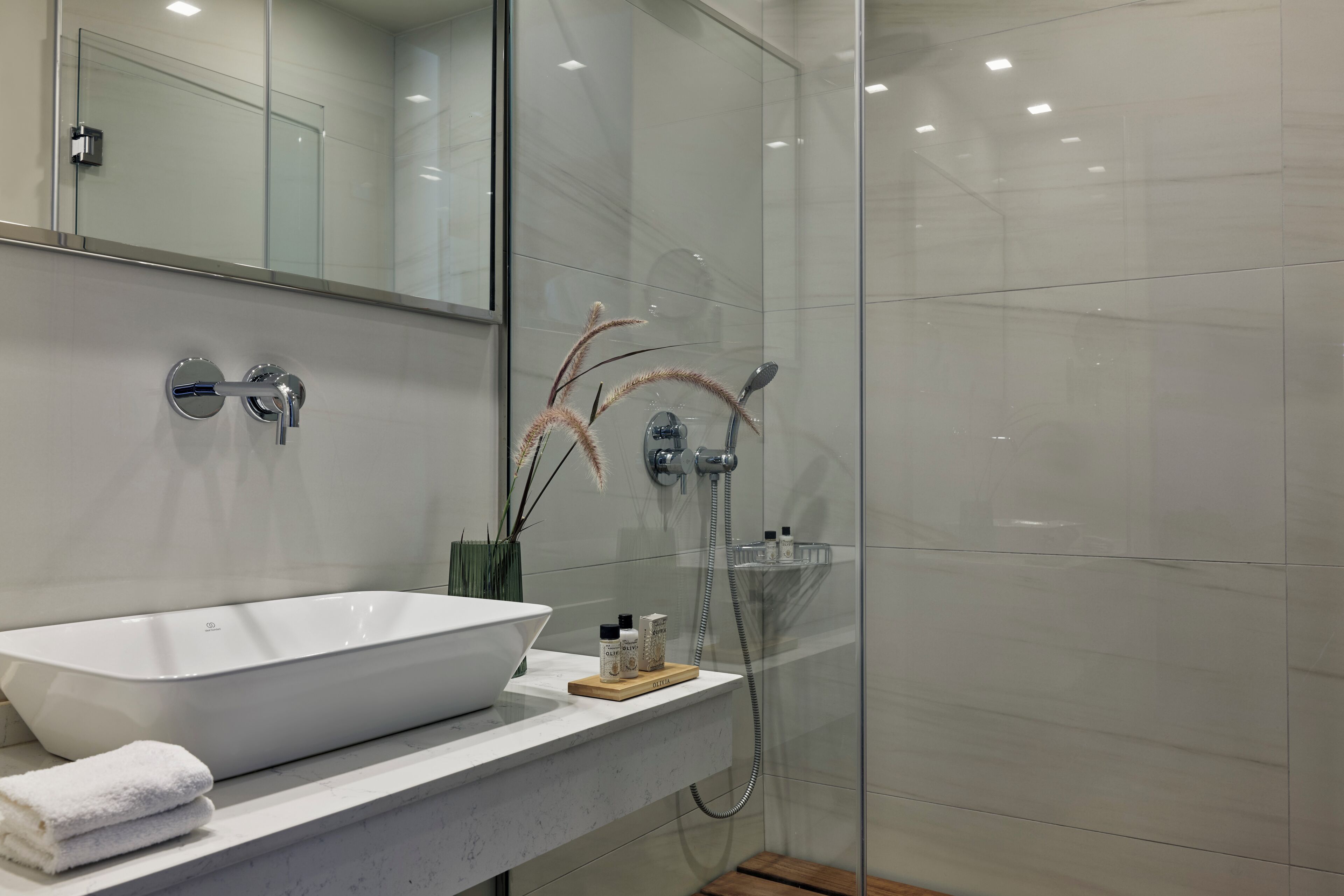 A modern bathroom with a large white vessel sink, a mirror above it, and a glass-enclosed shower area.