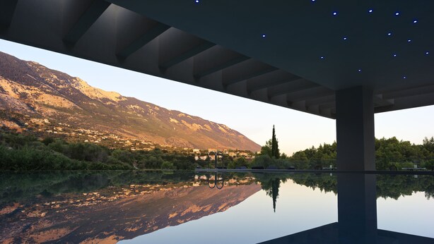 Uma estrutura arquitetônica moderna com uma piscina refletora, montanhas ao fundo e céu claro.
