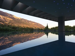 A modern architectural structure with a reflective pool, a mountain backdrop, and a clear sky.