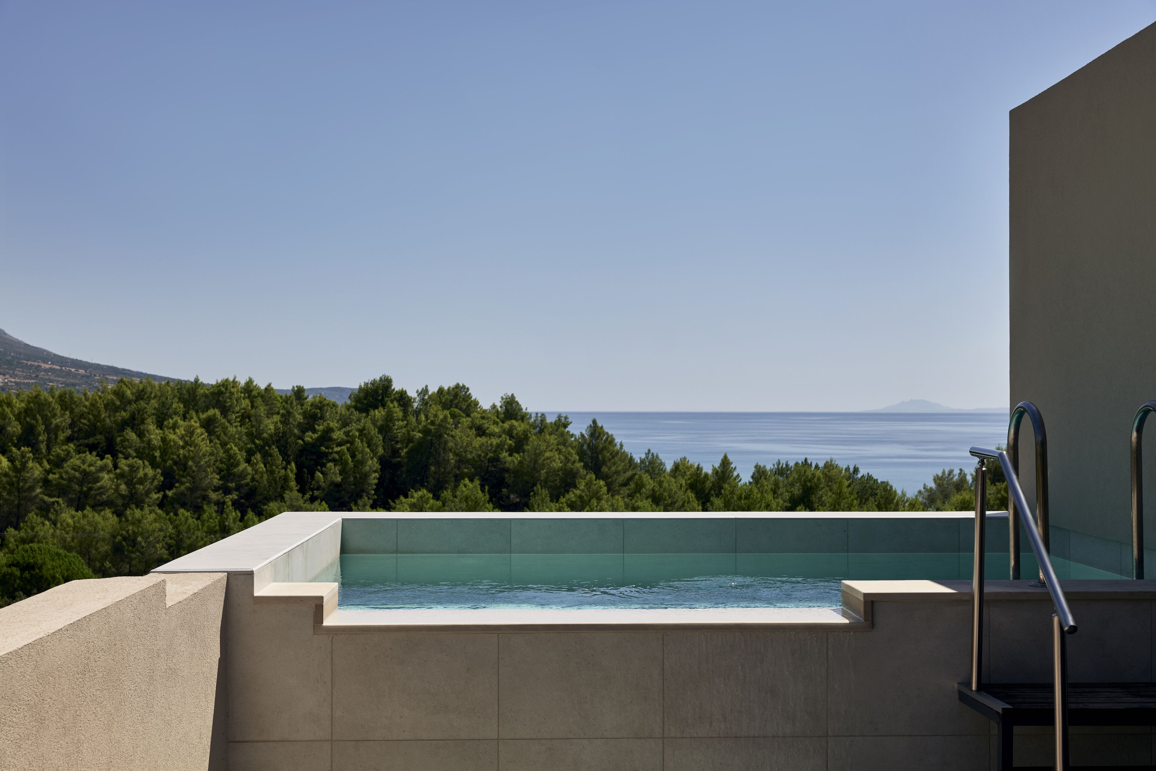Una piscina infinitum al terrat amb una vista despejada del mar i un paisatge de muntanyes al fons.