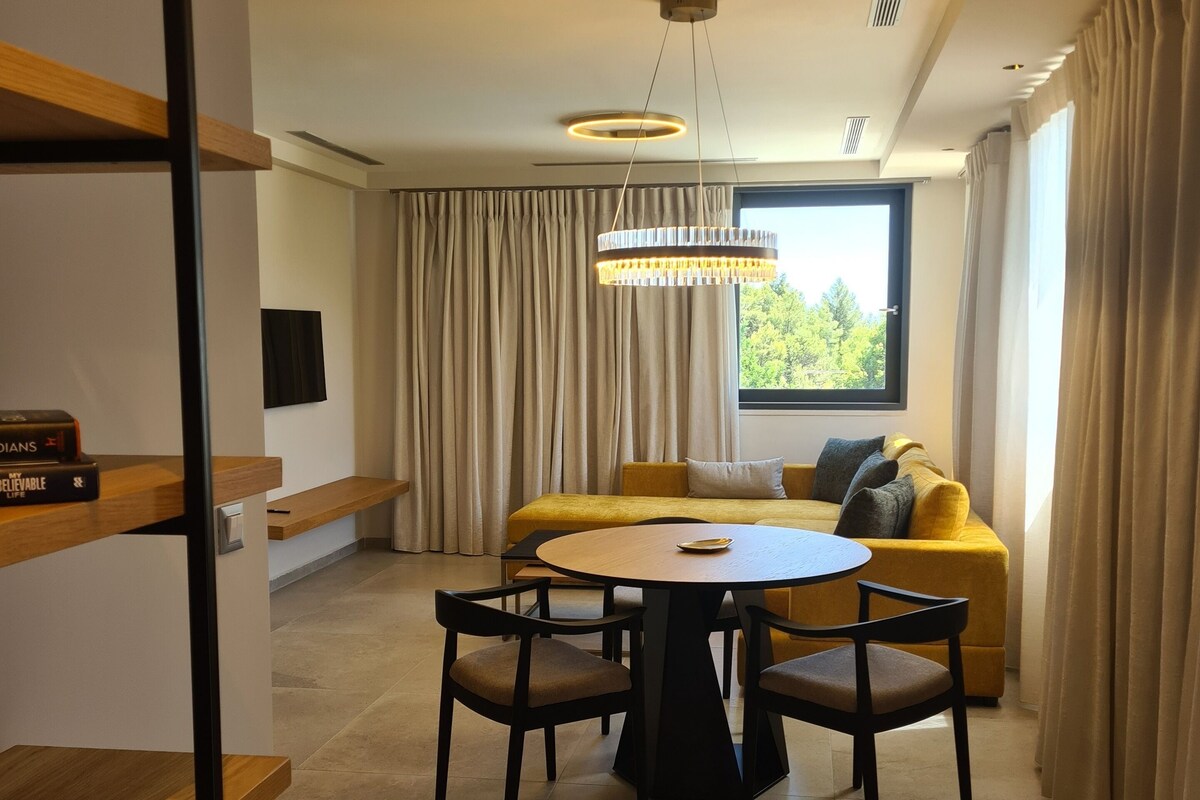 A modern living room with a round table, yellow sofa, and a large window with curtains.