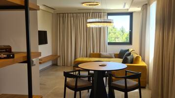 A modern living room with a round table, yellow sofa, and a large window with curtains.