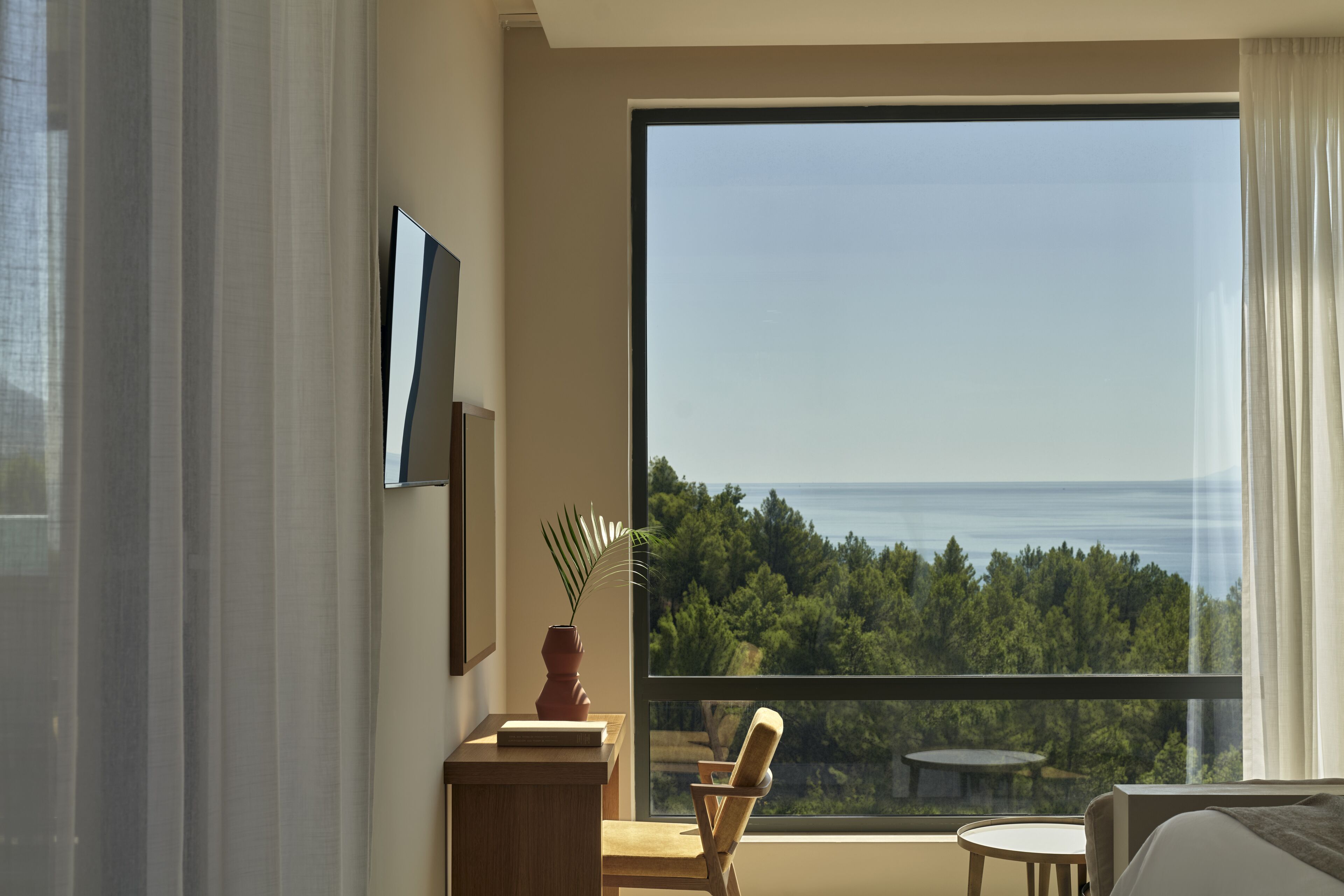 Una habitación de hotel moderna con un amplio ventanal que ofrece vistas a un bosque y al mar.
