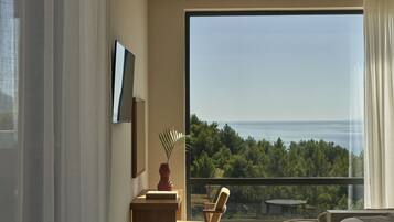 Una habitación de hotel moderna con un amplio ventanal que ofrece vistas a un bosque y al mar.
