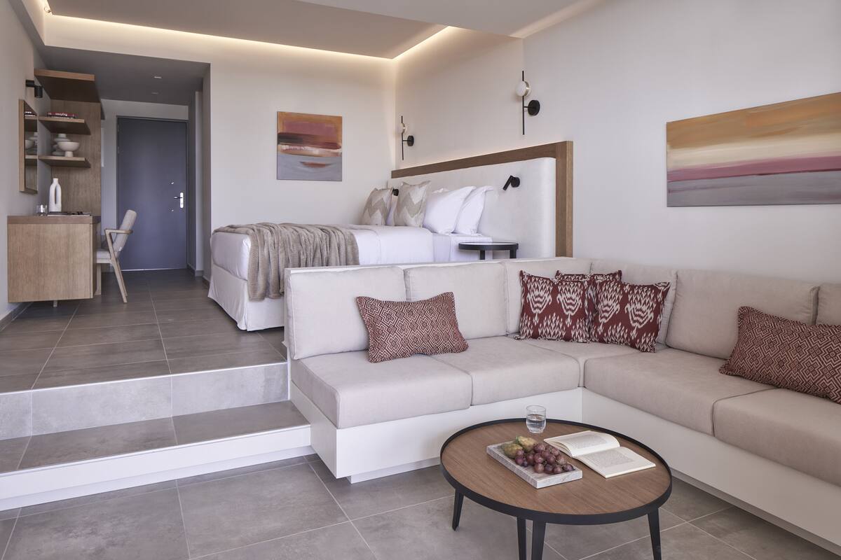 A modern living room with a sofa, coffee table, and a bed in the background.