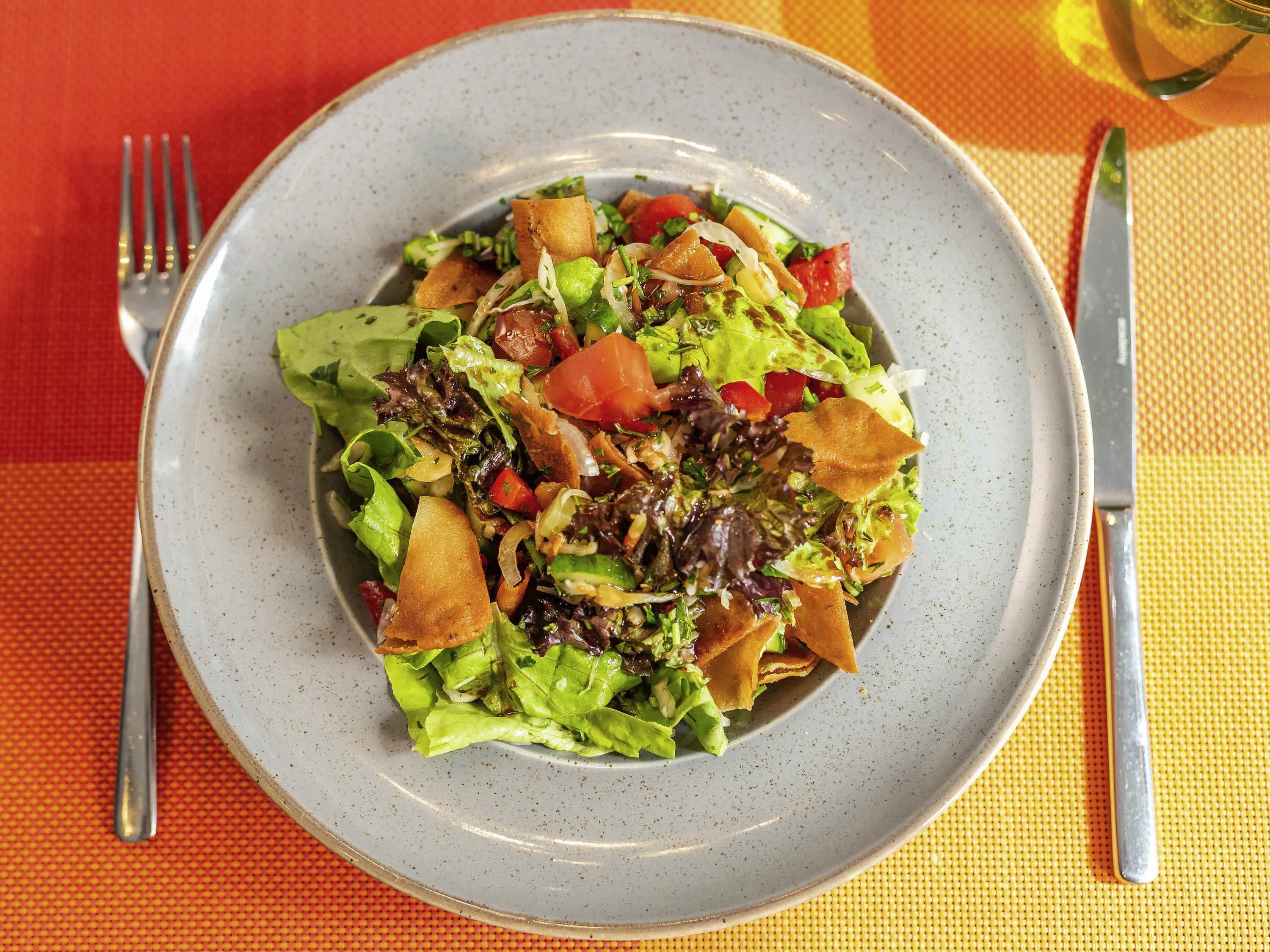 A plate of salad with various vegetables and a fork and knife on the table.