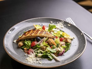 Ein Teller gegrilltes Hähnchen mit einem gemischten Salat auf einem dunklen Teller.