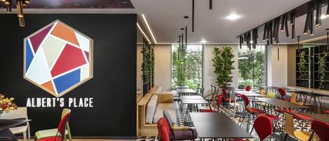 Interior de una cafetería moderna con un logotipo geométrico, suelo con estampado blanco y negro, y sillas rojas y verdes.