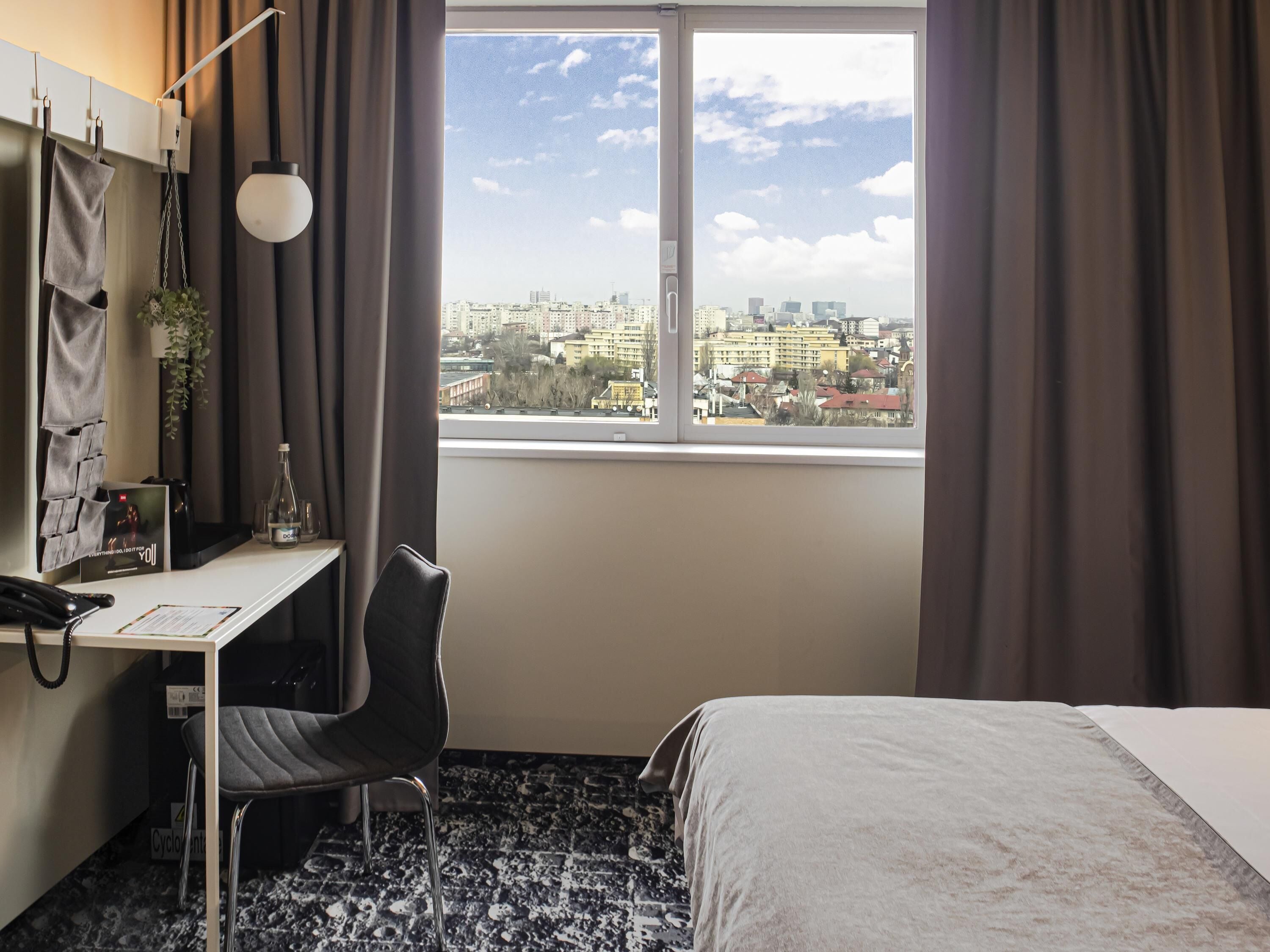 Habitación de hotel con escritorio, silla, cama y vista a la ciudad desde la ventana.