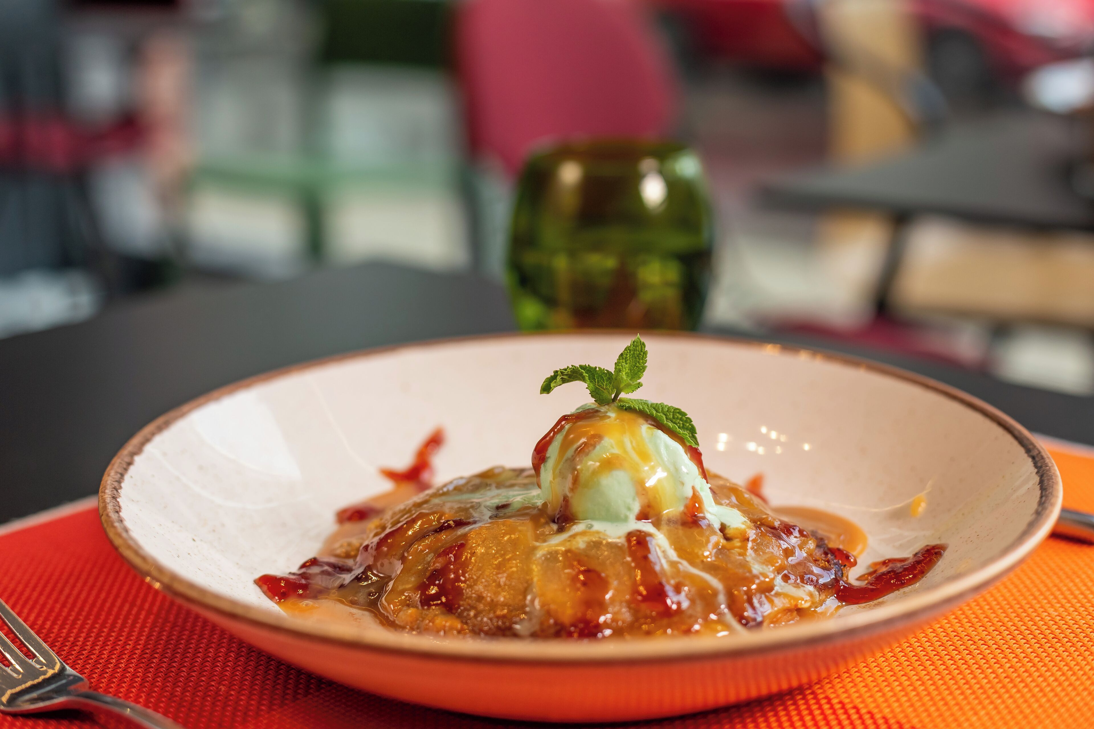 Un dessert servi dans une assiette, décoré d’une feuille de menthe, et posé sur un set de table rouge.