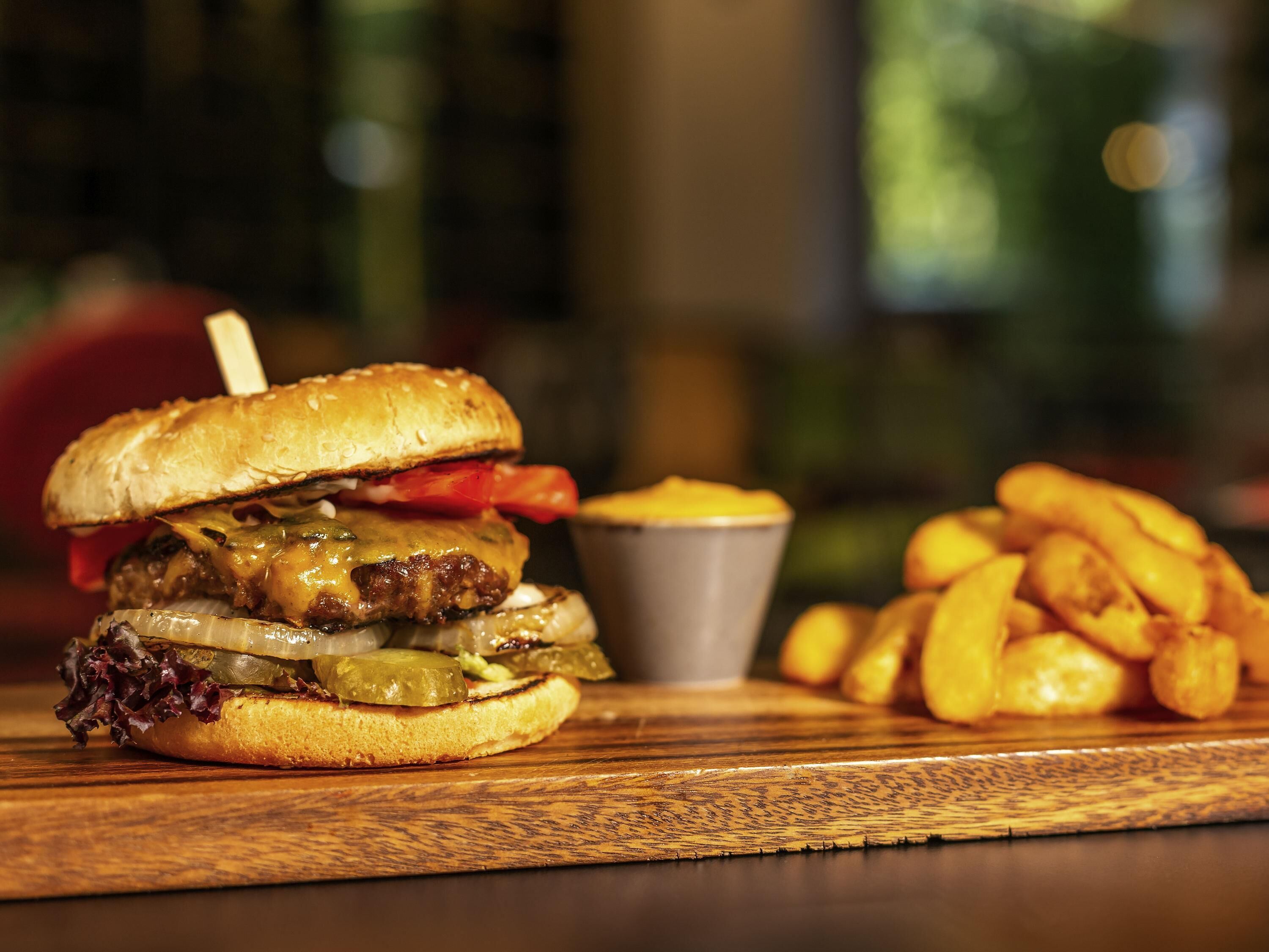 A burger with pickles, a small cup, and fries on a wooden table.