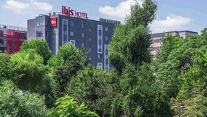 A modern hotel building with a prominent 'ibis HOTEL' sign, surrounded by lush greenery and parked cars. - ibis Bucharest Politehnica (Bucharest)